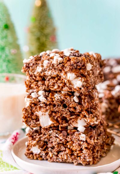 Close up photo of 3 chocolate rice krispie treats stacked on top of each other on a white plate.