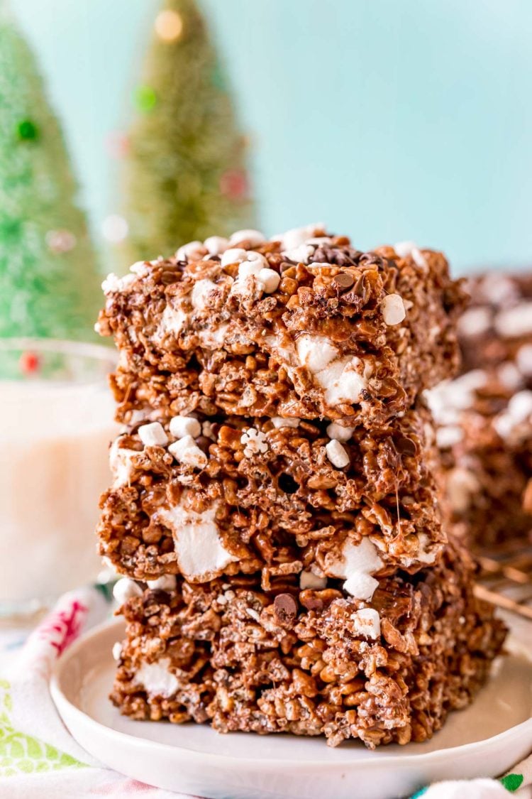 Close up photo of 3 chocolate rice krispie treats stacked on top of each other on a white plate.