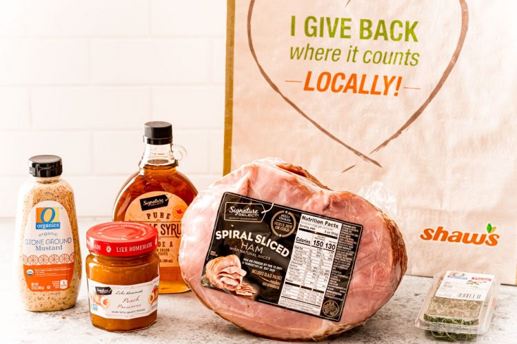 Ingredients to make a glazed ham on a white table with a reusable bag in the background.