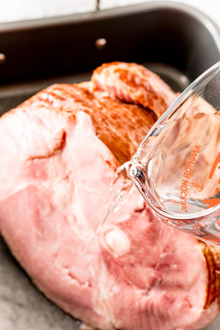 Water being poured into a roasting pan with a ham in it.