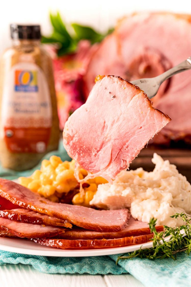 A slice of ham being held over a plate with a fork.