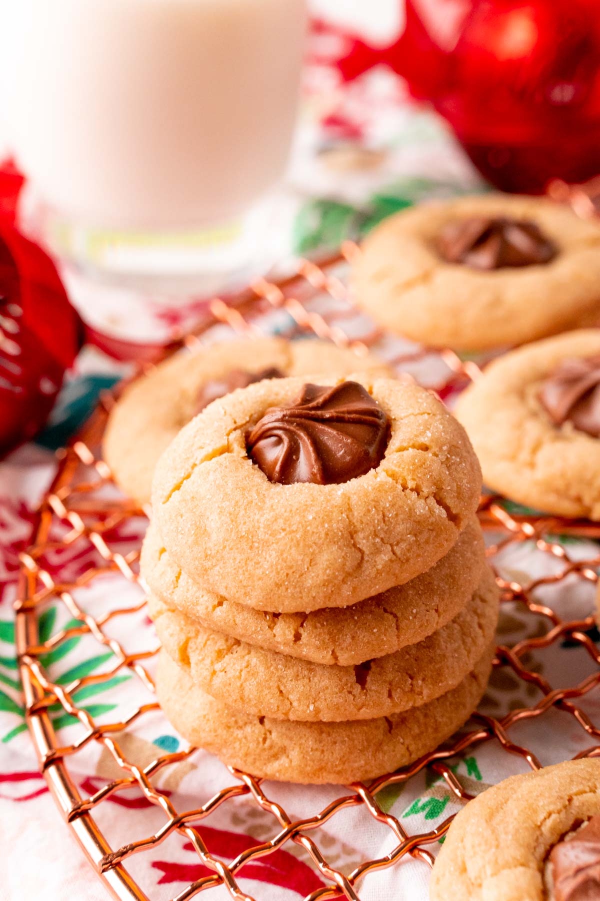 A stack of 4 peanut butter blossom cookies on a copper wire rack with a glass of milk in the background.