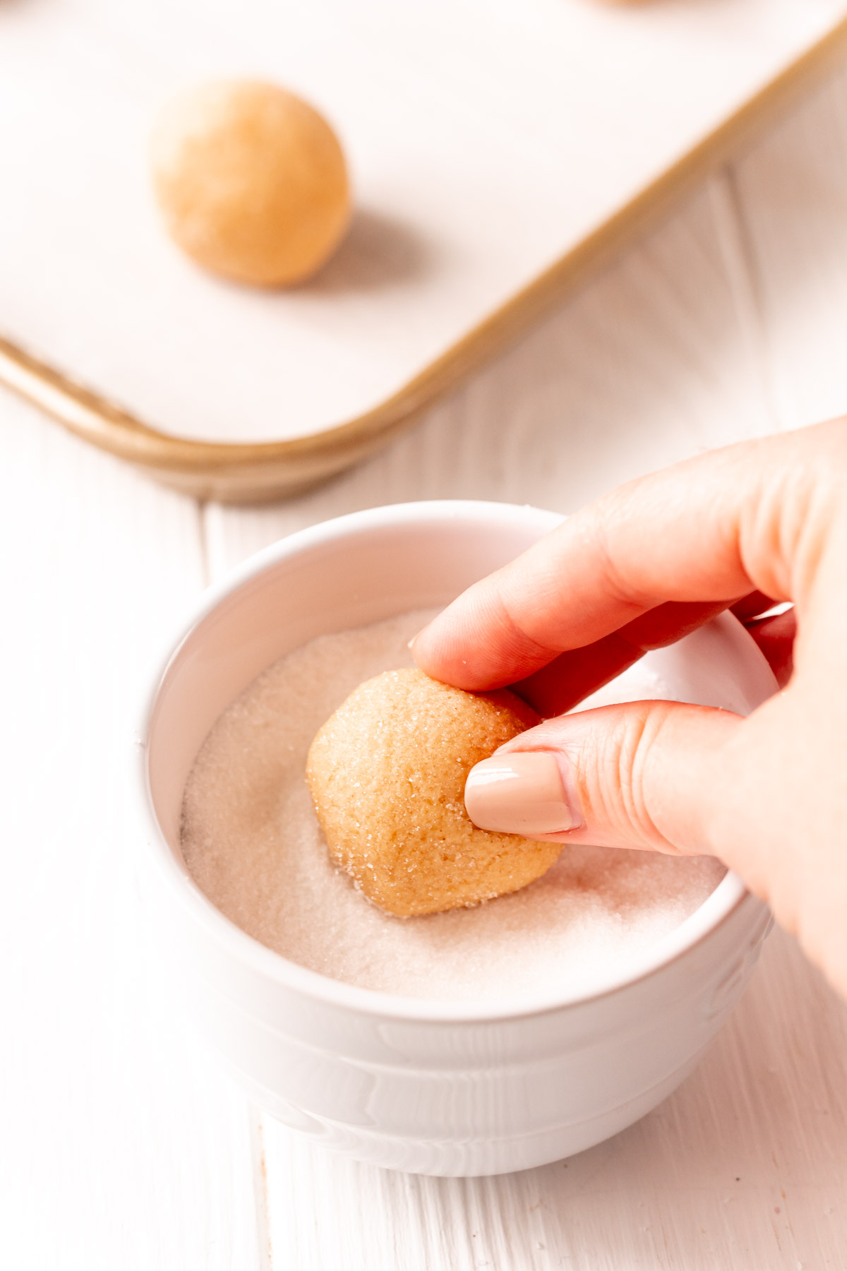 peanut butter cookies dough ball being rolls in a white bowl of granulated sugar.