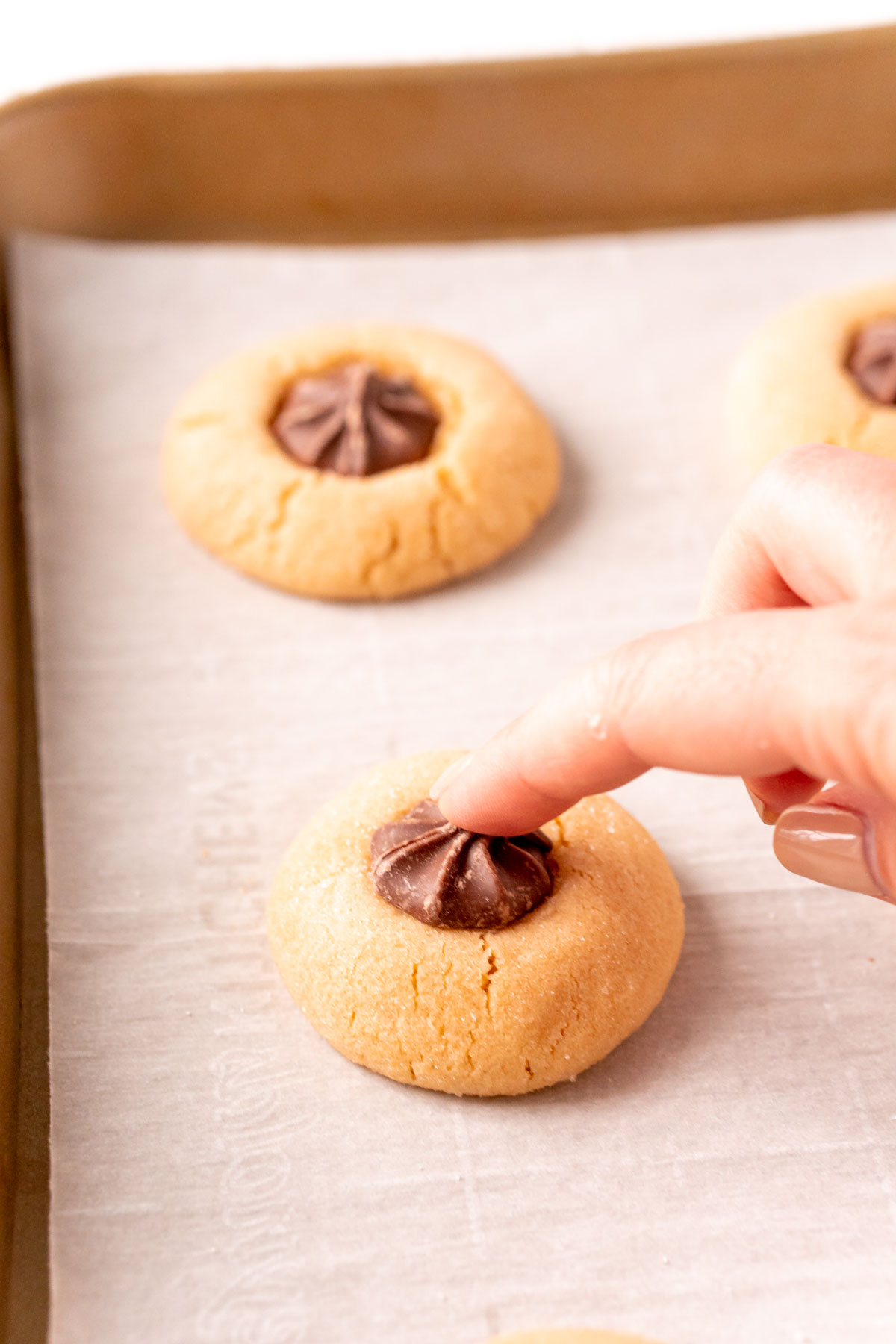 A chocolate candy star being pressed into a peanut butter cookie on a baking sheet.