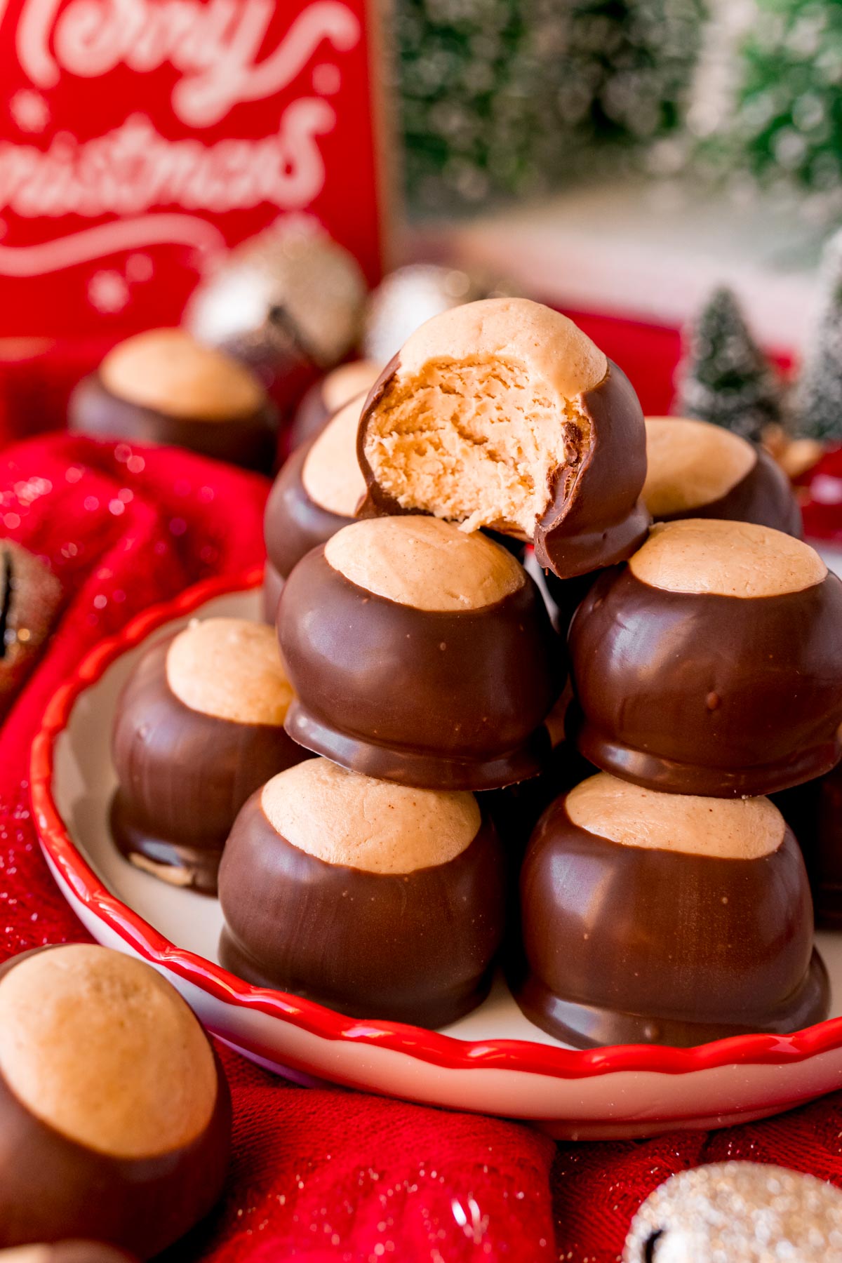 Close up photo of a plate of peanut butter buckeyes with the one on top with a bit missing surrounded by holiday decorations.