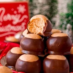 Close up photo of a plate of peanut butter buckeyes with the one on top with a bit missing surrounded by holiday decorations.