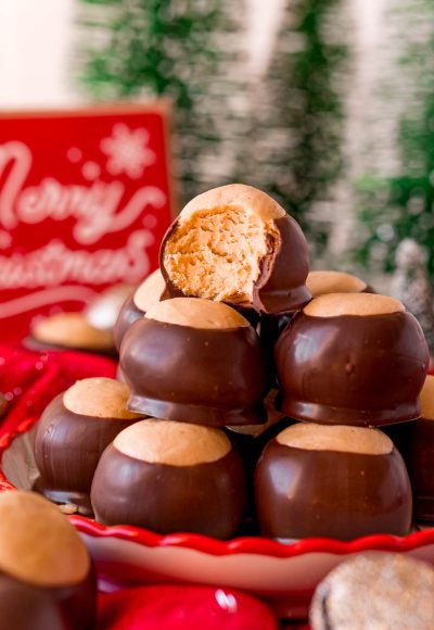 Close up photo of a plate of peanut butter buckeyes with the one on top with a bit missing surrounded by holiday decorations.