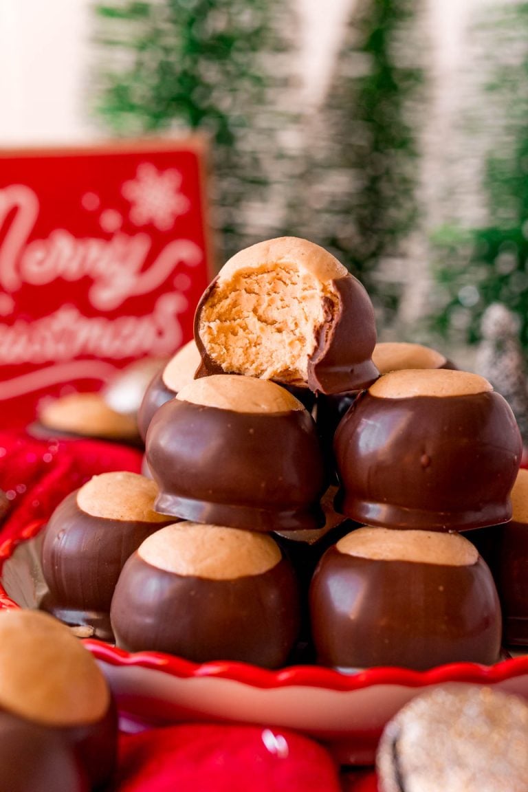 Close up photo of a plate of peanut butter buckeyes with the one on top with a bit missing surrounded by holiday decorations.