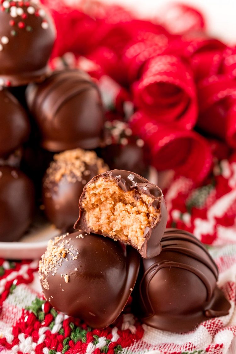 Three nutter butter balls stacked in a pyramid with the top one missing a bite. A plate with more balls and holiday decorations is behind it.