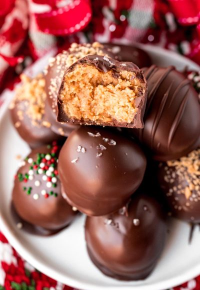 Close up photo of a stack of peanut butter balls on a white plate. The top one has a bite taken out of it.