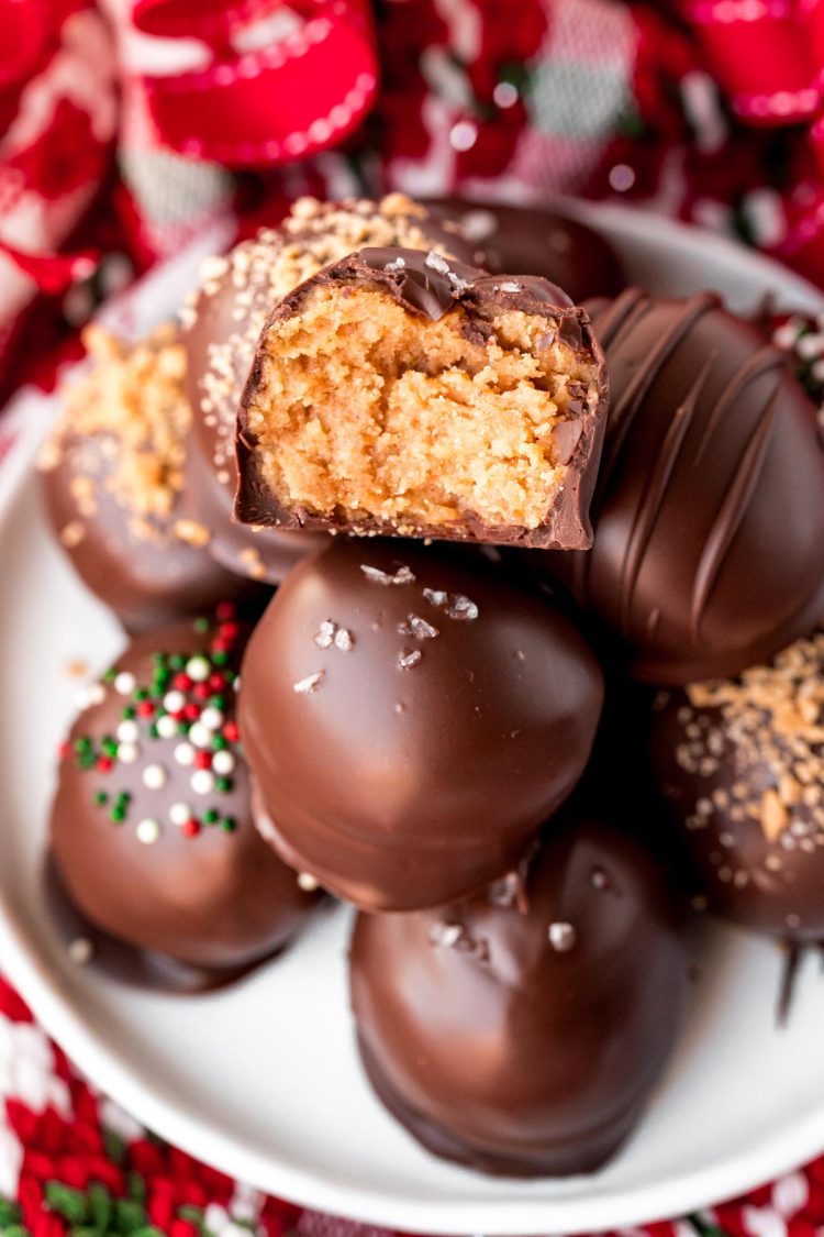 Close up photo of a stack of peanut butter balls on a white plate. The top one has a bite taken out of it.