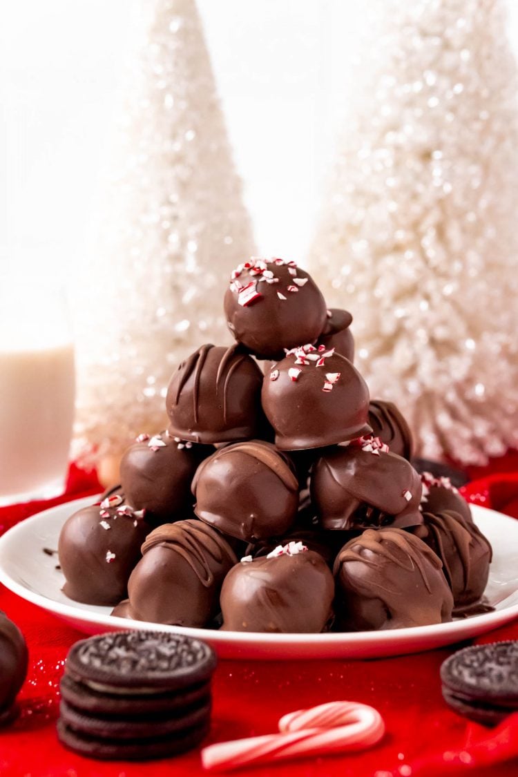 A pile of oreo balls on a white plate with holiday decorations around them.