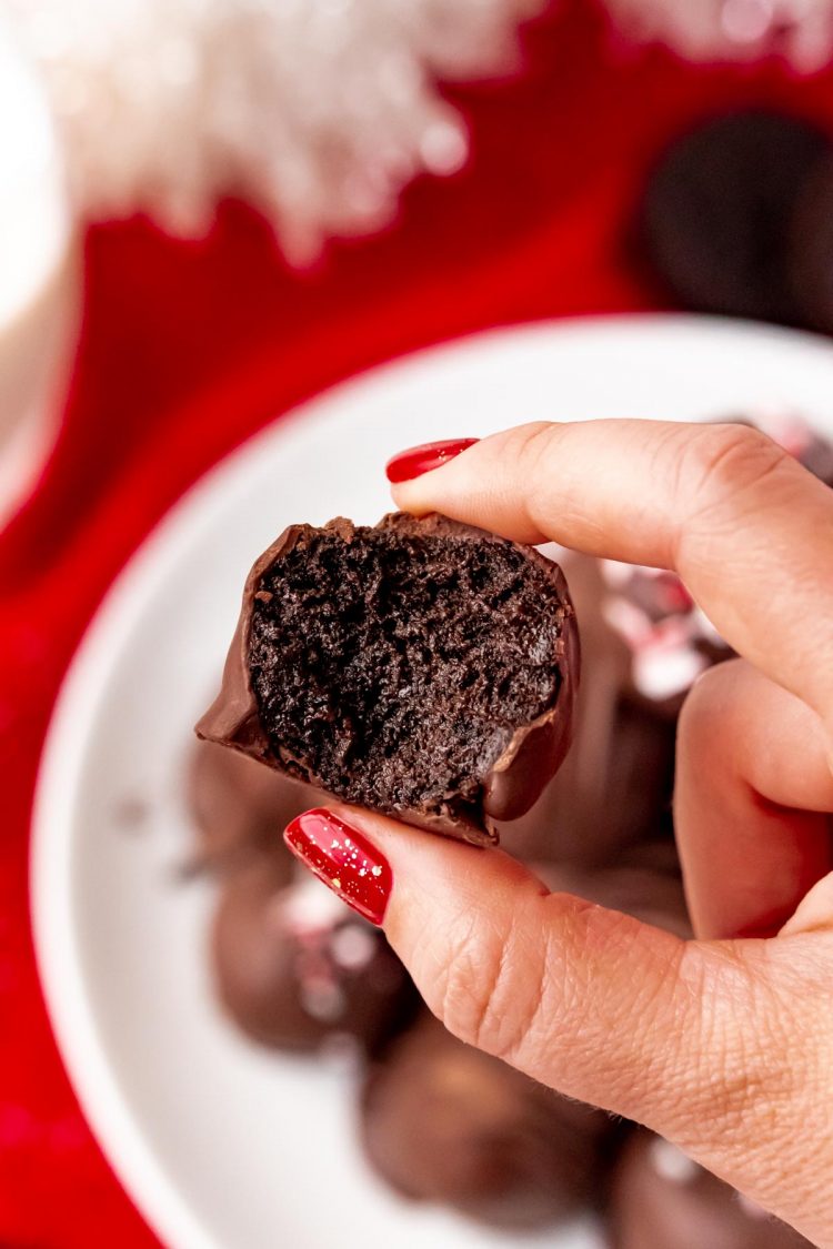 Woman's hand holding an Oreo ball to the camera with a bite taken out of it.