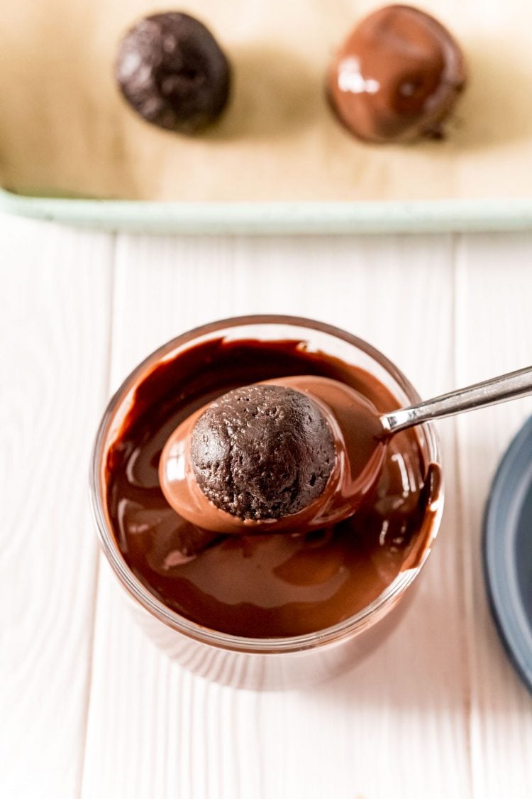 A spoon dipping an oreo ball in chocolate.