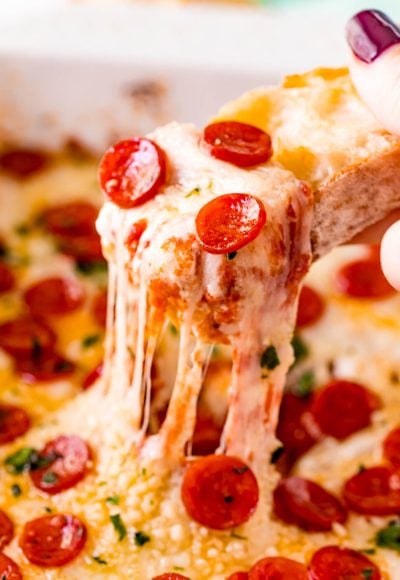 A piece of baguette scooping pizza dip our of a white baking dish.