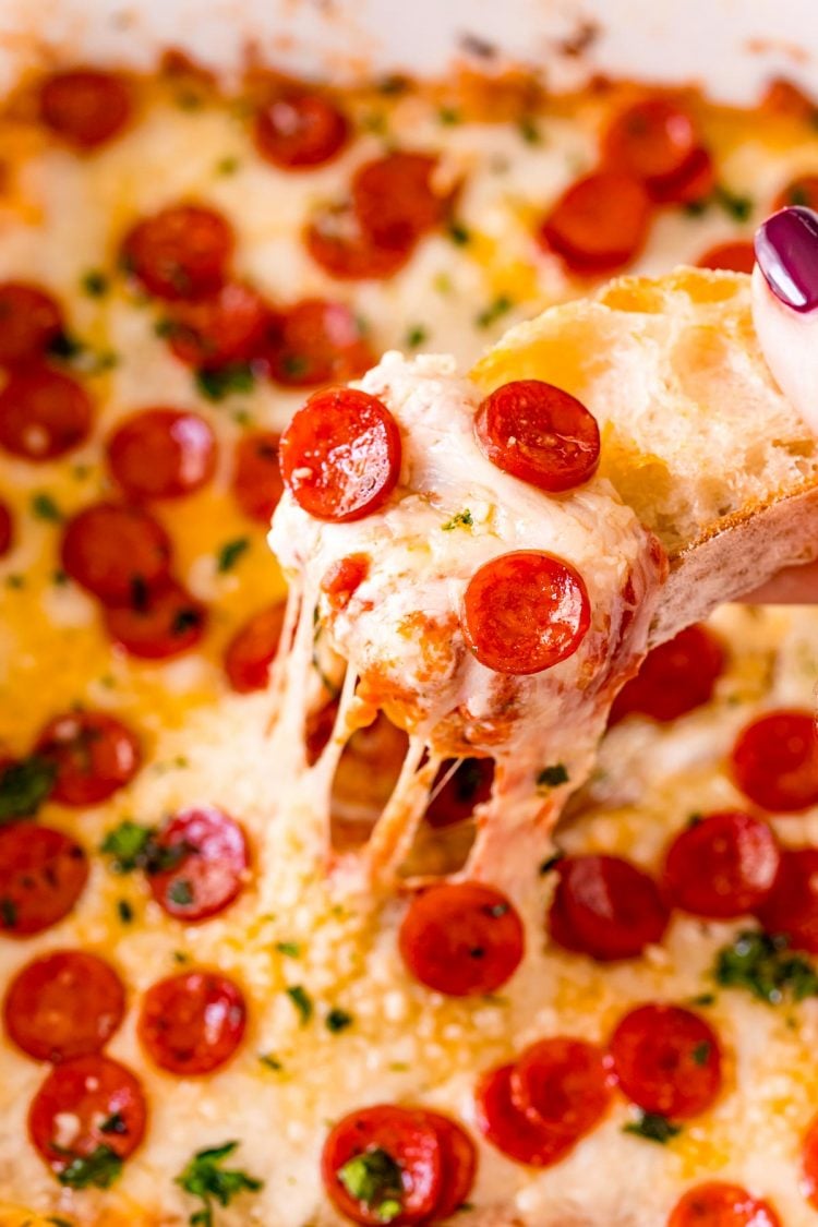 Close up photo of a piece of bread scooping pepperoni pizza dip.