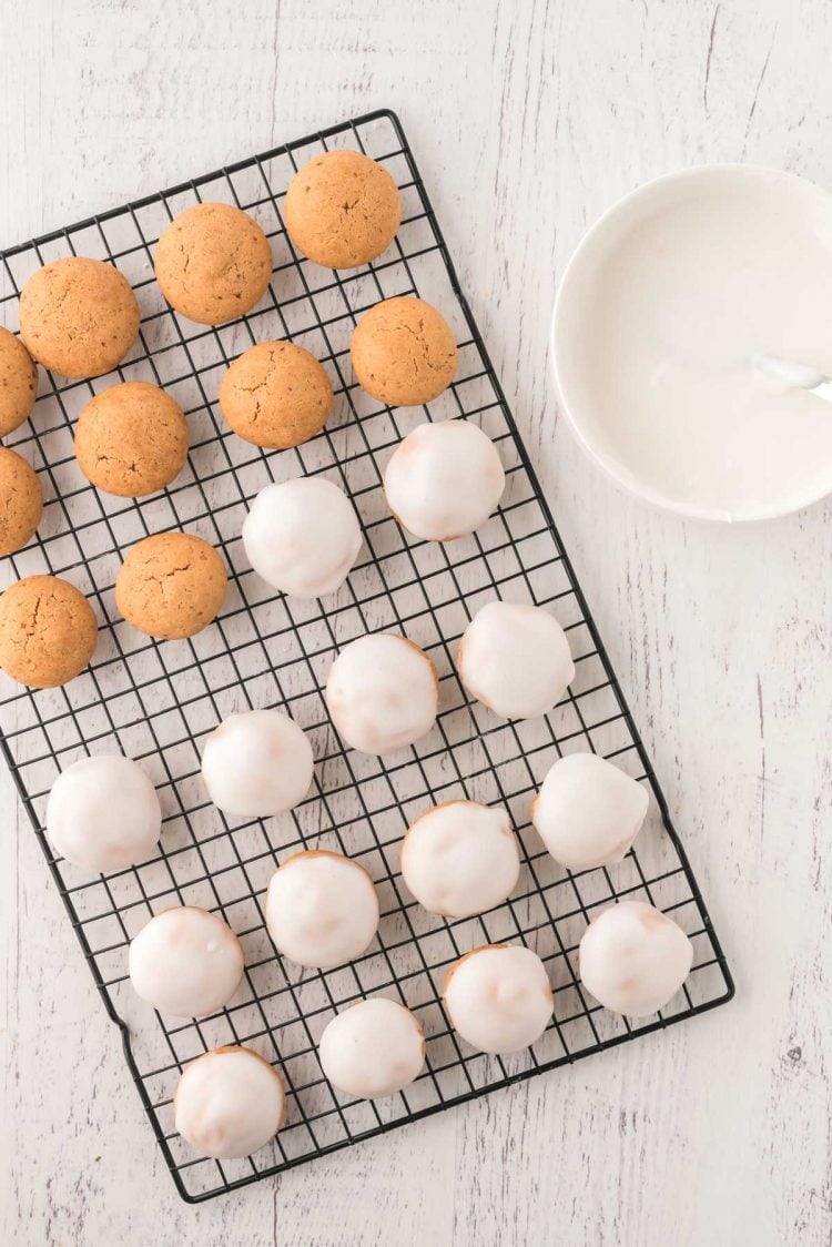 Cookies on a wire rack some iced, some not. Bowl of icing to the side.