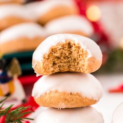 Close up photo of three pfeffernusse cookies stacked on op of each other with holiday decorations in the background.