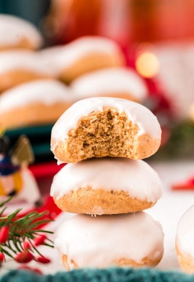 Close up photo of three pfeffernusse cookies stacked on op of each other with holiday decorations in the background.