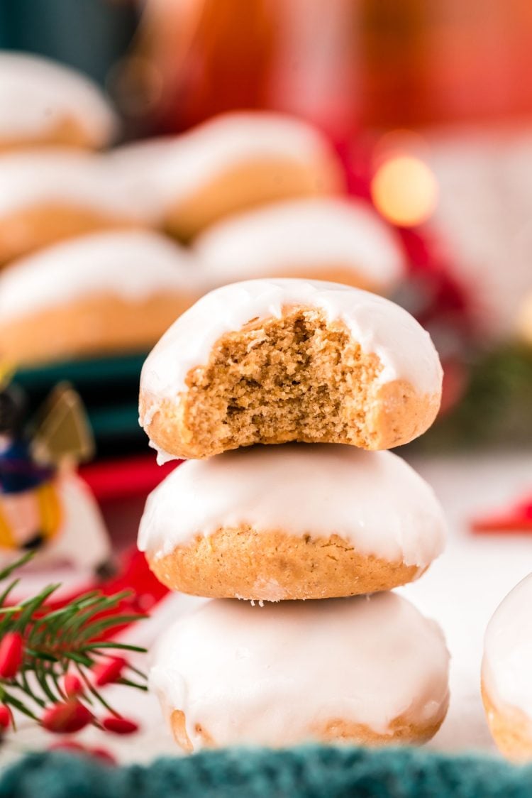 Close up photo of three pfeffernusse cookies stacked on op of each other with holiday decorations in the background.