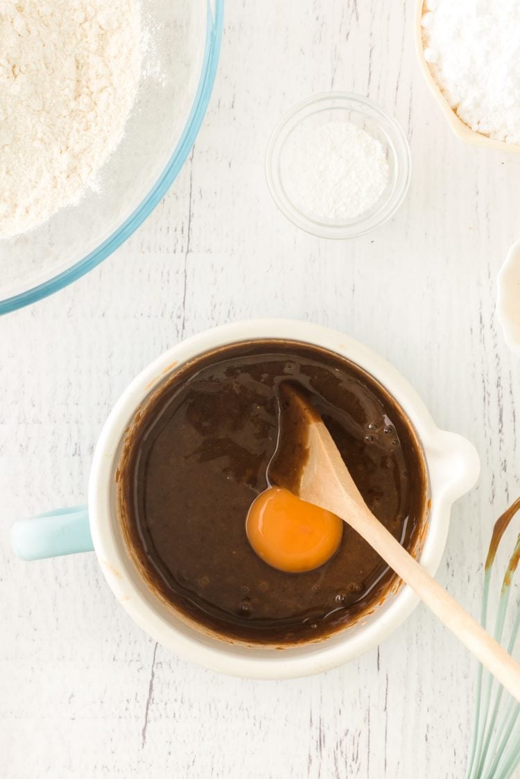 Egg being added into a pot with honey and brown sugar that has been melted.