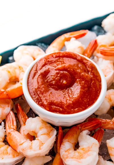 Close up photo of cocktail sauce in a small white bowl on top of a platter of shrimp and ice.