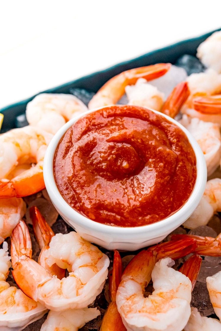 Close up photo of cocktail sauce in a small white bowl on top of a platter of shrimp and ice.