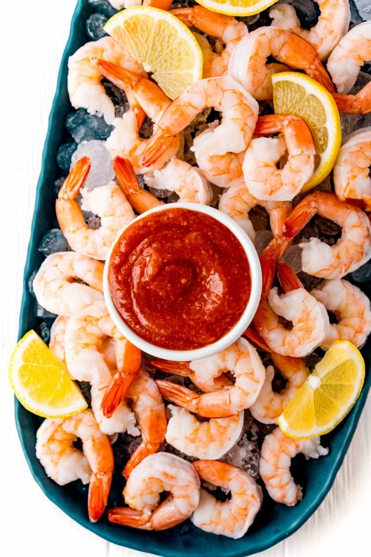 Overhead photo of shrimp cocktail on a blue platter with ice.