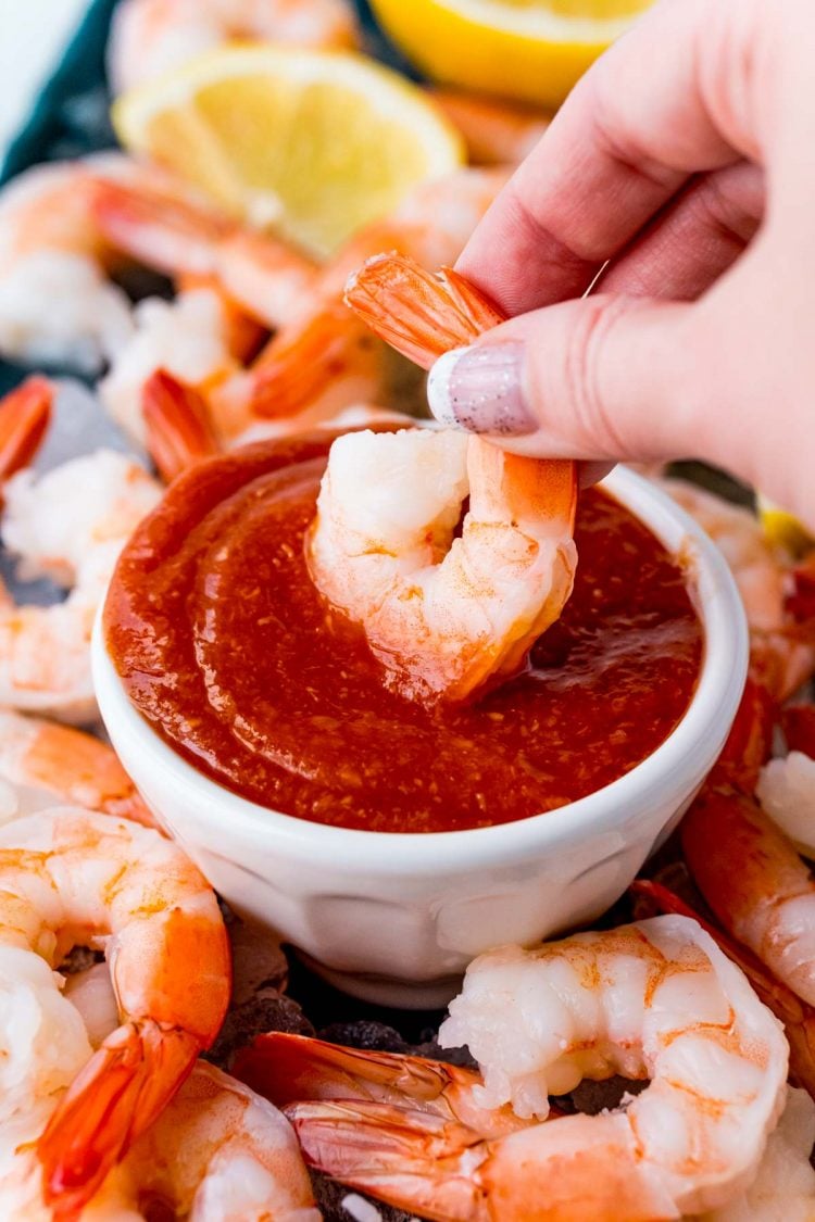 A woman's hand dipping a shrimp in cocktail sauce.