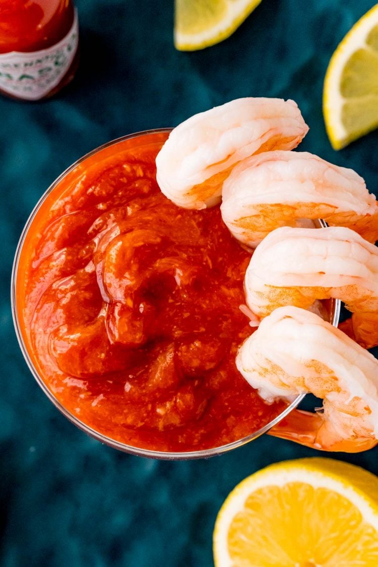 Overhead photo of a serving glass with cocktail sauce in it and shrimp hanging on the side.