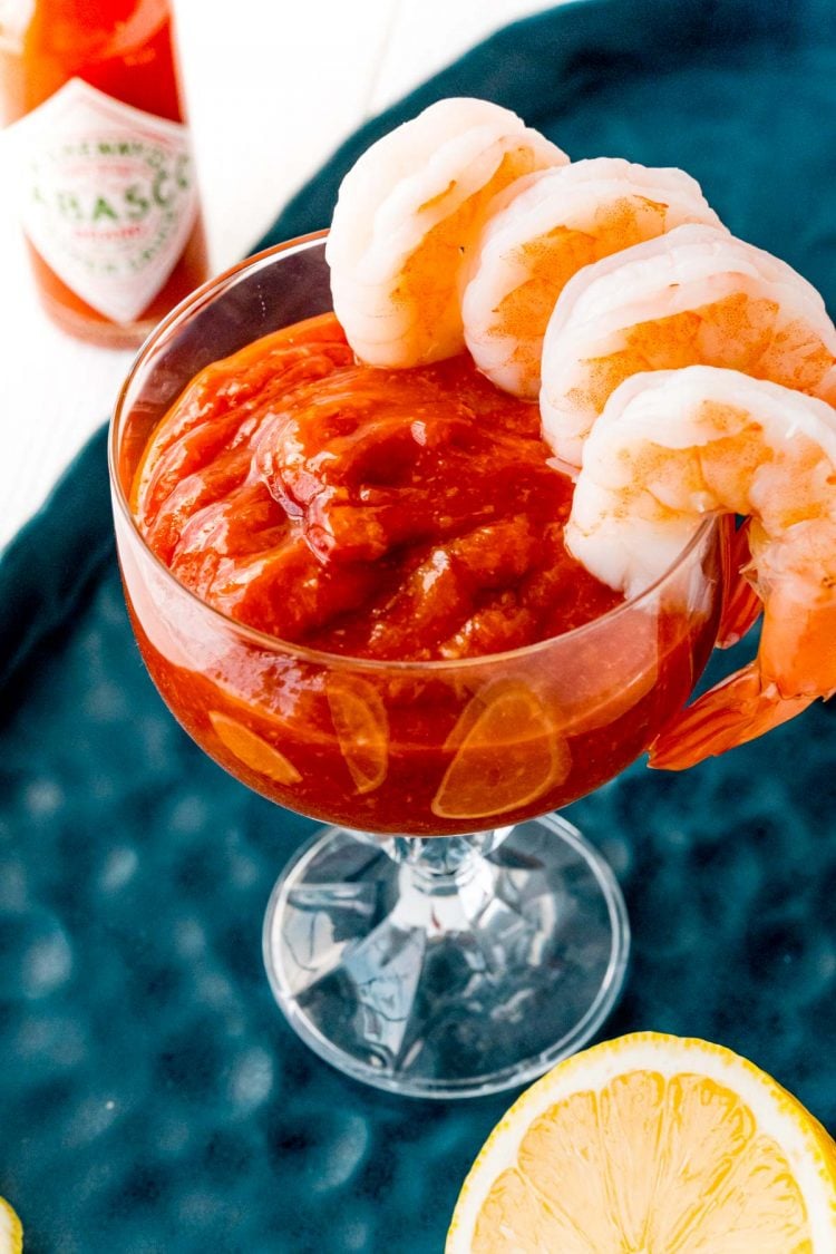 Shrimp hanging from a glass with cocktail sauce in it.