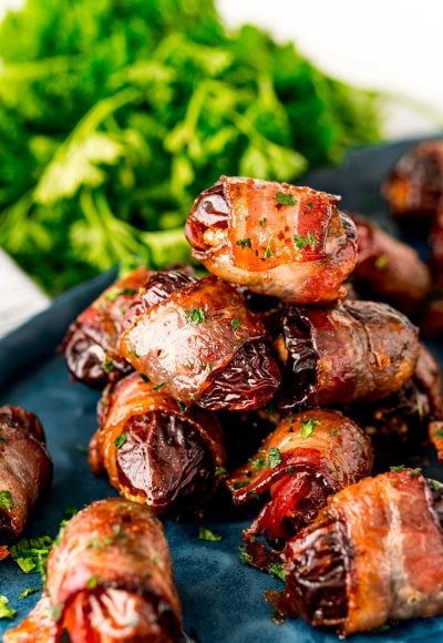 Close up photo of bacon wrapped dates piled on top of each other on a blue plate.