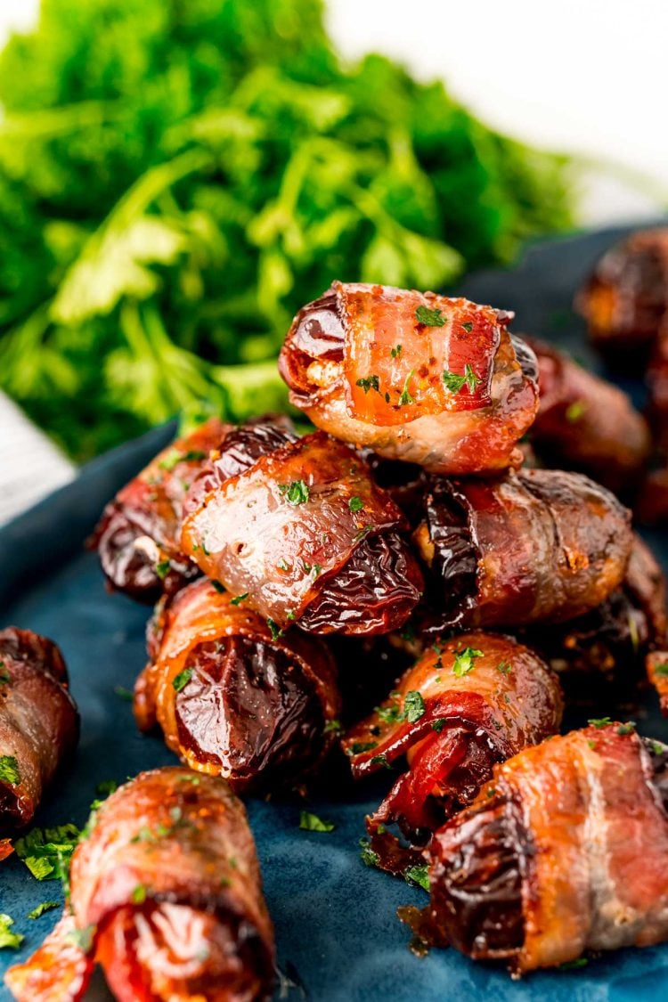 Close up photo of bacon wrapped dates piled on top of each other on a blue plate.