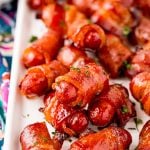 Close up photo of bacon wrapped little smokies on a white serving tray.