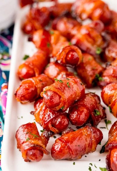 Close up photo of bacon wrapped little smokies on a white serving tray.