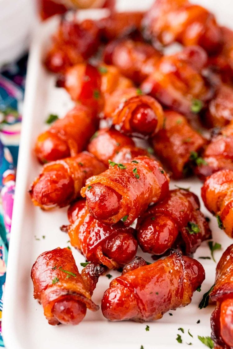 Close up photo of bacon wrapped little smokies on a white serving tray.