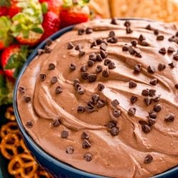 Close up photo of a blue bowl with brownie batter dip in it with pretzels, strawberries and cookies around it.