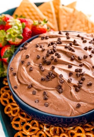 Close up photo of a blue bowl with brownie batter dip in it with pretzels, strawberries and cookies around it.