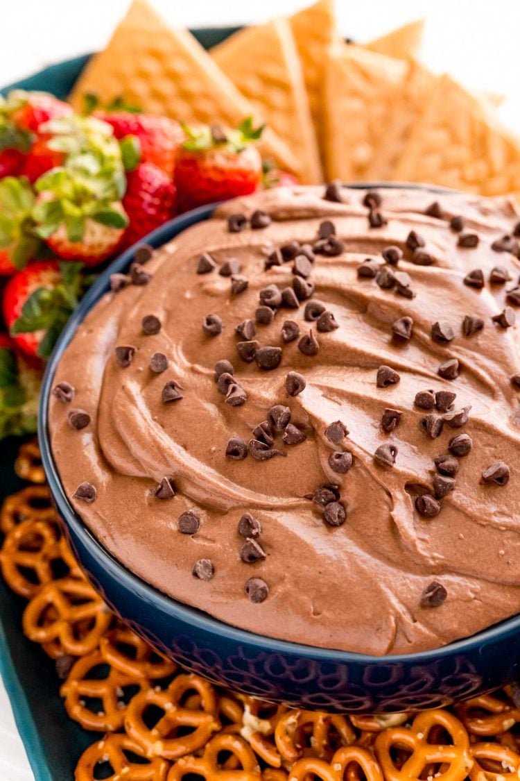 Close up photo of a blue bowl with brownie batter dip in it with pretzels, strawberries and cookies around it.