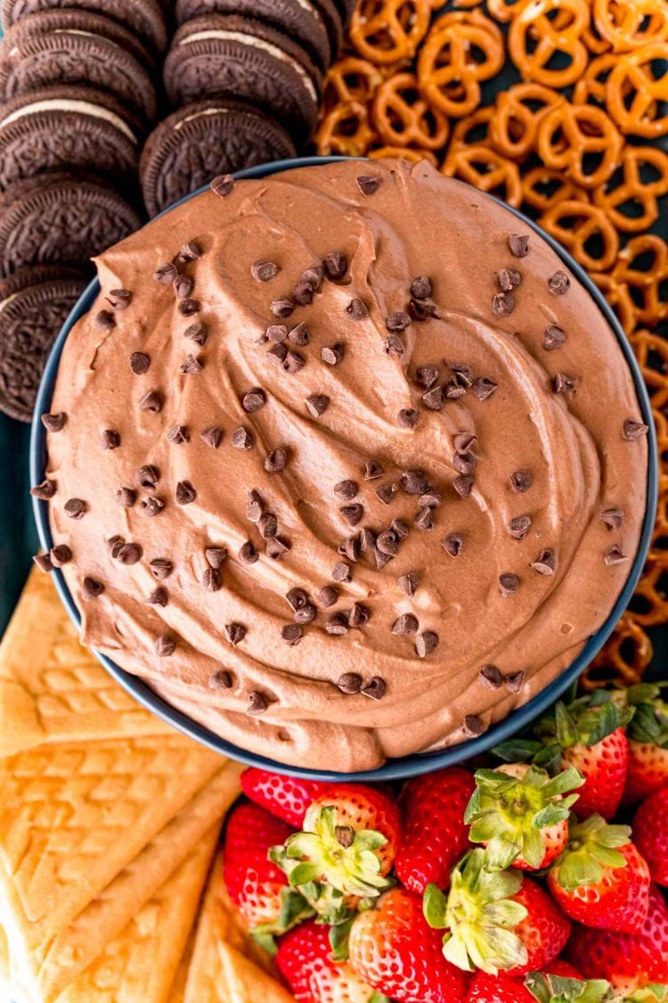 Overhead photo of a bowl of brownie dip topped with chocolate chips and surrounded by fruits and cookies.