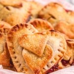 Heart shaped hand pies in a basket with a pink and white striped napkin.
