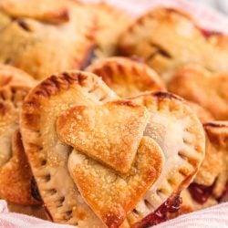 Heart shaped hand pies in a basket with a pink and white striped napkin.