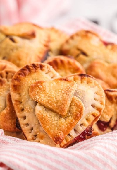 Heart shaped hand pies in a basket with a pink and white striped napkin.