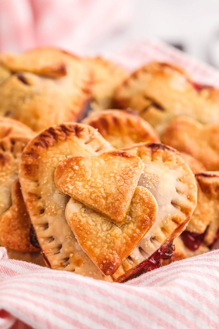 Heart shaped hand pies in a basket with a pink and white striped napkin.