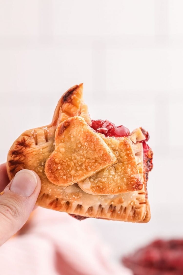 A woman's hand holding a heart shaped cherry hand pie.