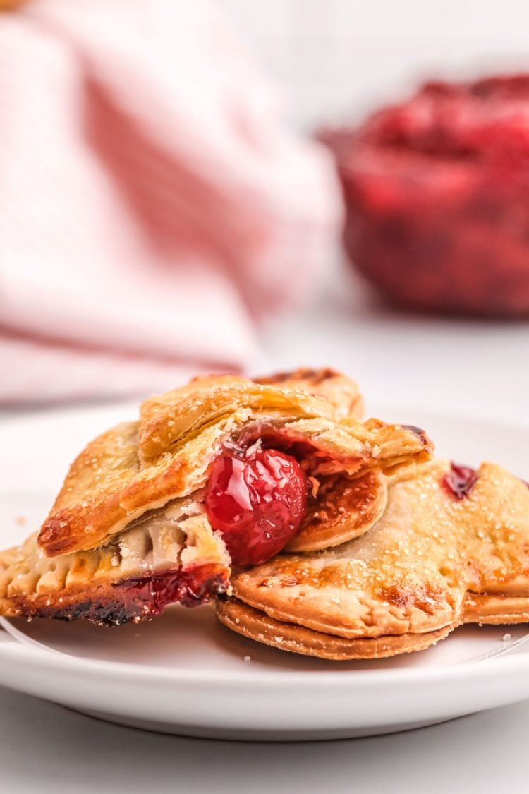 Close up photo of cherry hand pies on a plate, one has a bite taken out of it.