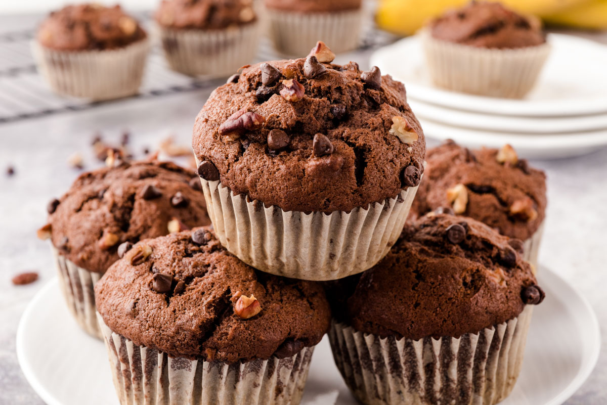 Chocolate chip banana muffins piled on top of each other on a white plate.