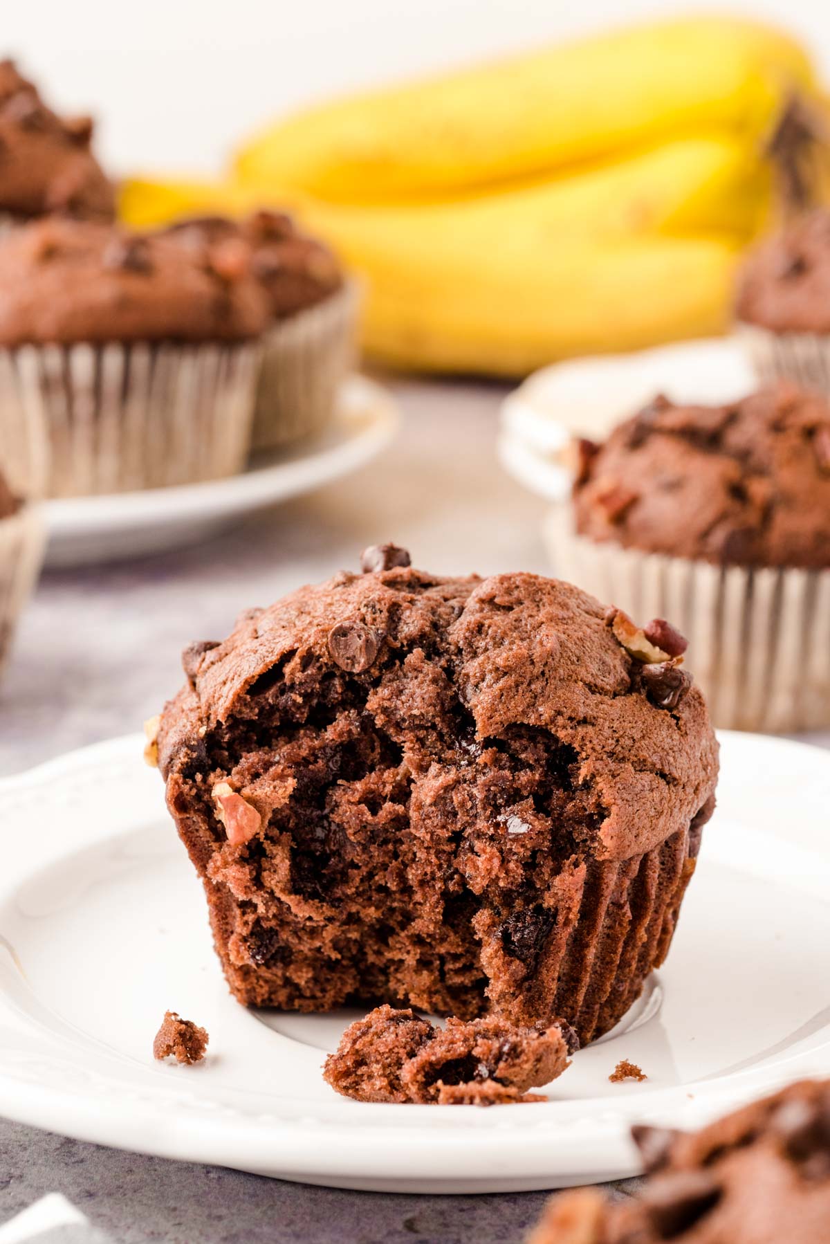 A chocolate banana muffin on a white plate with a bite missing.