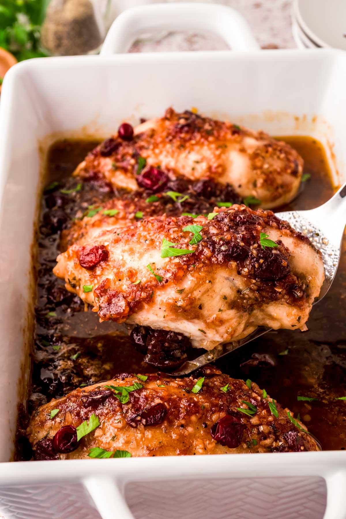 A spatula lifting a cranberry chicken breast out of a baking dish.