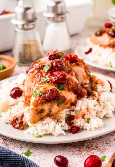 Close up photo of cranberry chicken on a bed of rice on a white plate.